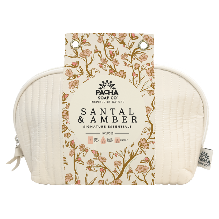 The Self Care Spa Set - Santal & Amber by Pacha Soap Co. includes soap, body wash, bath bomb, and candle in a cream-colored quilted pouch with a floral tag. Enjoy a woodsy scent for the perfect self-care gift set.