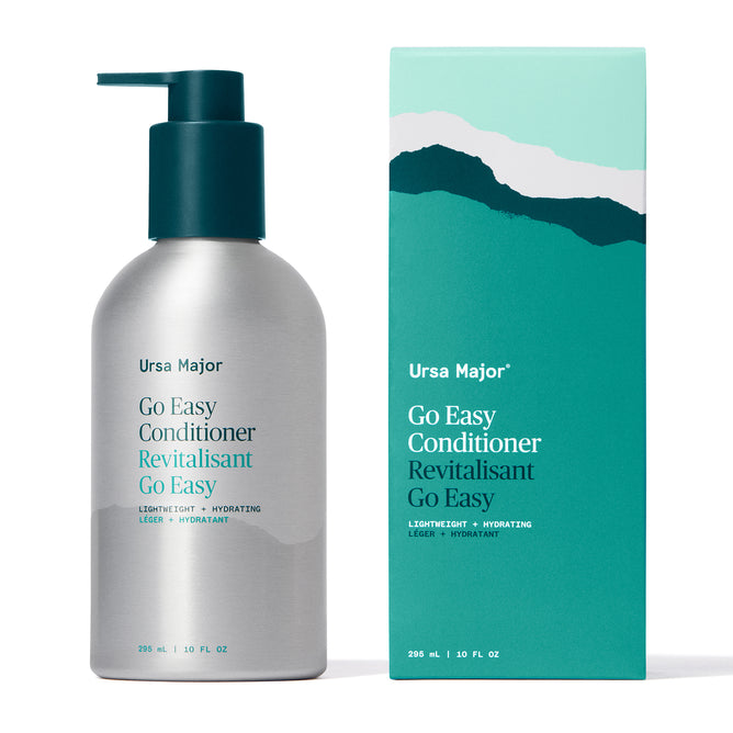 A silver pump bottle and teal box of Ursa Major Go Easy Conditioner, both 296 mL (10 fl oz), feature a minimalist mountain design and highlight its lightweight, hydrating formula for added shine.