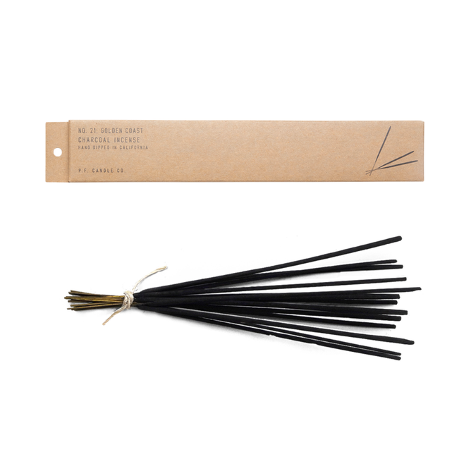 A bundle of black Incense Sticks from P.F. Candle Co., tied with twine, is positioned beneath a brown rectangular box on a white background, evoking signature scents with rich sandalwood notes.