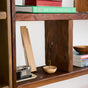 Wooden shelves display books, a red box, a film camera, a stack of magazines, and incense sticks by P.F. Candle Co. in a small wooden bowl, filling the air with their signature sandalwood scent and creating a cozy, organized interior scene.
