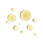 Several translucent yellow drops of Ursa Majors Golden Hour Dry Oil are scattered on a white background, illustrating how this dry-finish oil locks in moisture and helps replenish both skin and hair.