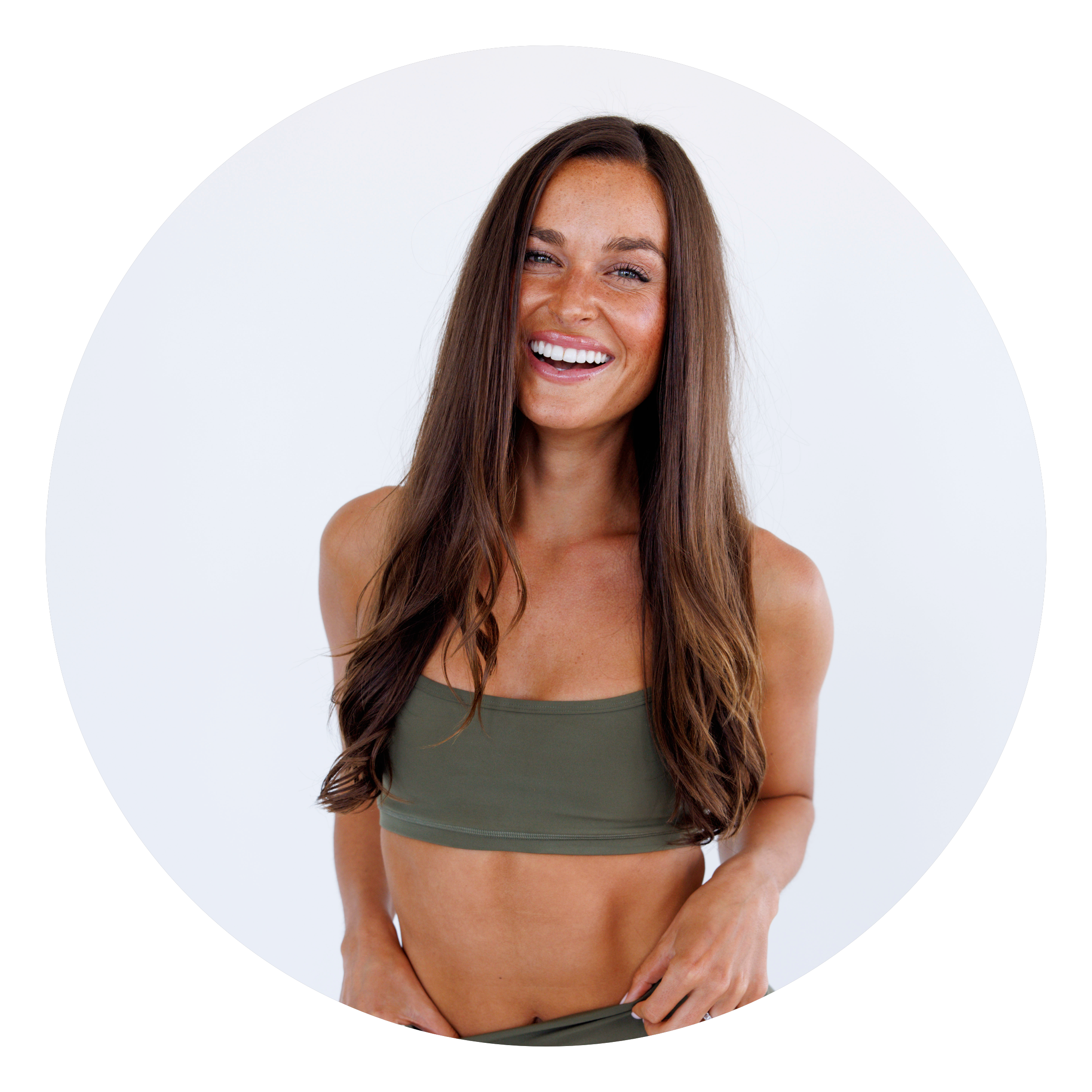 A woman with long brown hair wearing a green sports bra and matching bottoms smiles at the camera against a plain white background.