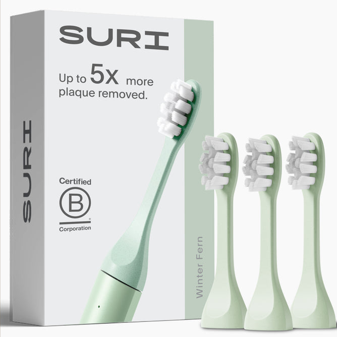 SURI’s 3x Brush Replacement Heads, shown with a light green plant-based toothbrush in Winter Fern—ideal for sensitive teeth and gums. Box features: “Up to 5x more plaque removed.” All heads are recyclable. Brand: SURI.