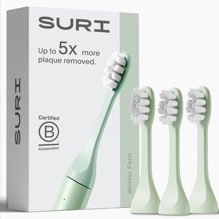 SURI’s 3x Brush Replacement Heads, shown with a light green plant-based toothbrush in Winter Fern—ideal for sensitive teeth and gums. Box features: “Up to 5x more plaque removed.” All heads are recyclable. Brand: SURI.