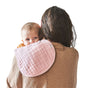 A baby wearing a Green Sprouts 100% Certified Organic Cotton Muslin Burp Cloth in light pink rests on an adults shoulder. The hypoallergenic fabric provides comfort as the baby looks at the camera, with the adult in a brown sweater facing away against a clean white backdrop.