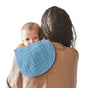 A baby cuddles on a womans shoulder who has long brown hair and is wearing a brown sweater. The baby, looking at the camera, is wrapped in a Green Sprouts 100% Certified Organic Cotton Muslin Burp Cloth against a plain white background.