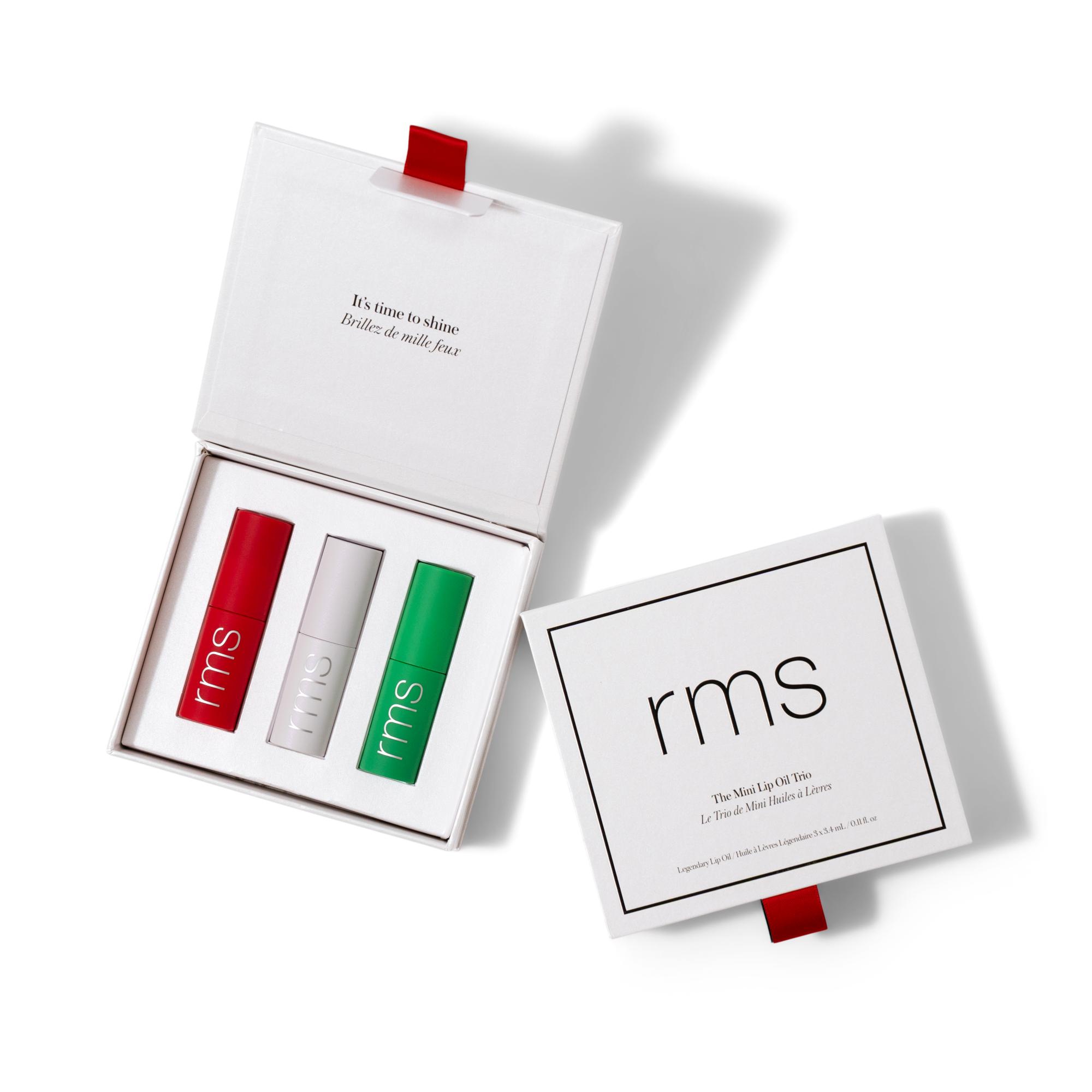 An open white box with a red ribbon reveals three tubes labeled rms in red, white, and green. Next to it is the closed lid reading rms and The Mini Lip Set Trio on a white background.