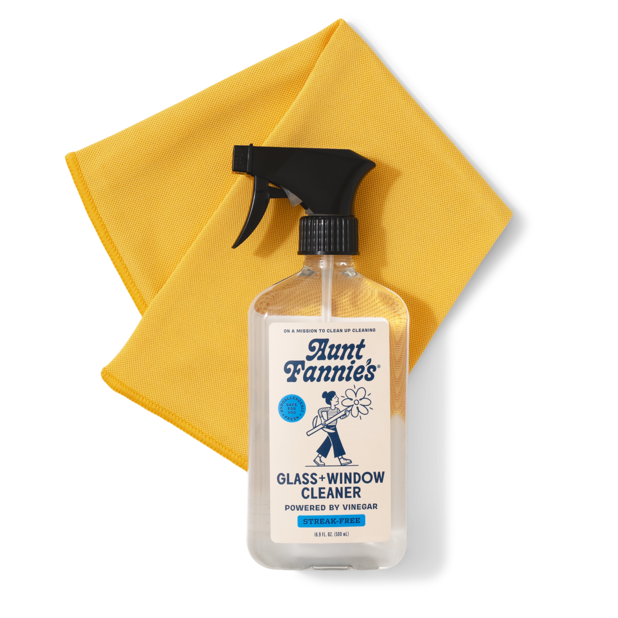A clear spray bottle labeled Aunt Fannies Glass & Window Cleaner with a black trigger sits on a yellow cleaning cloth. The cleaner is powered by vinegar and is streak-free.
