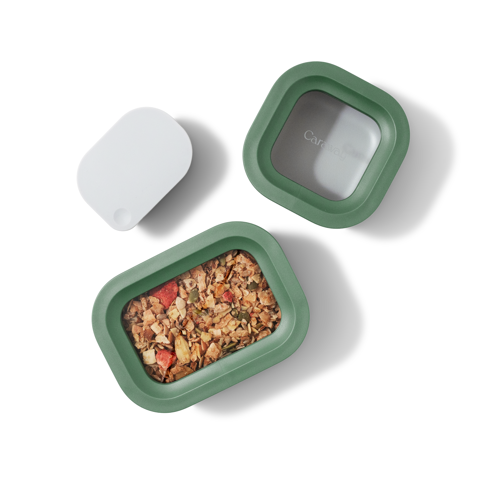 A green rectangular food container with a transparent lid is filled with granola. The lid is placed next to the container, along with a separate white accessory. All items are on a white background.