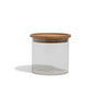 The Grove Co. Glass + Bamboo Storage Jar, featuring a clear cylindrical glass body and a flat, round bamboo lid, is displayed empty against a white background with a faint shadow to the left.