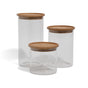 Three Grove Co. Glass + Bamboo Storage Jars of different heights, each featuring a round bamboo lid, are arranged side by side on a white background.