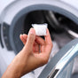 A hand holds a Grove Co. Laundry Detergent Pack (45 count) in front of an open washing machine filled with clothes.