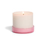 A lit Grove Co. Candle - 7oz in a simple round container with a pink base is photographed against a white background.