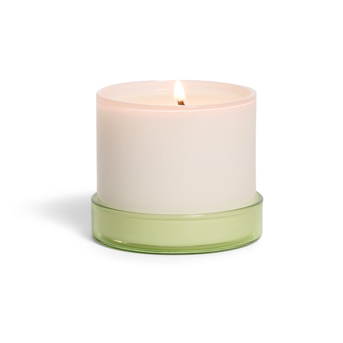 The Grove Co. Candle - 7oz is a lit white candle in a simple opaque container with a light green glass base, displayed against a white background.