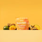 Blume SuperBelly Probiotic Hydration Powder in Mango Passion Fruit flavor features orange packaging surrounded by fresh mangoes and passion fruits, highlighting gut-supporting superfoods in a vivid tropical display against an orange background.