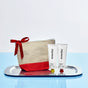A beige and red zippered pouch with a red ribbon sits on a silver tray next to two white tubes of Everist’s The Haircare Meets Skincare Set, set against a light blue and white background.