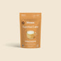 A brown pouch labeled blume Organic Salted Caramel Latte Powder is shown with a glass mug latte. This maca-infused, caffeine-free superfood offers 25 servings per package.
