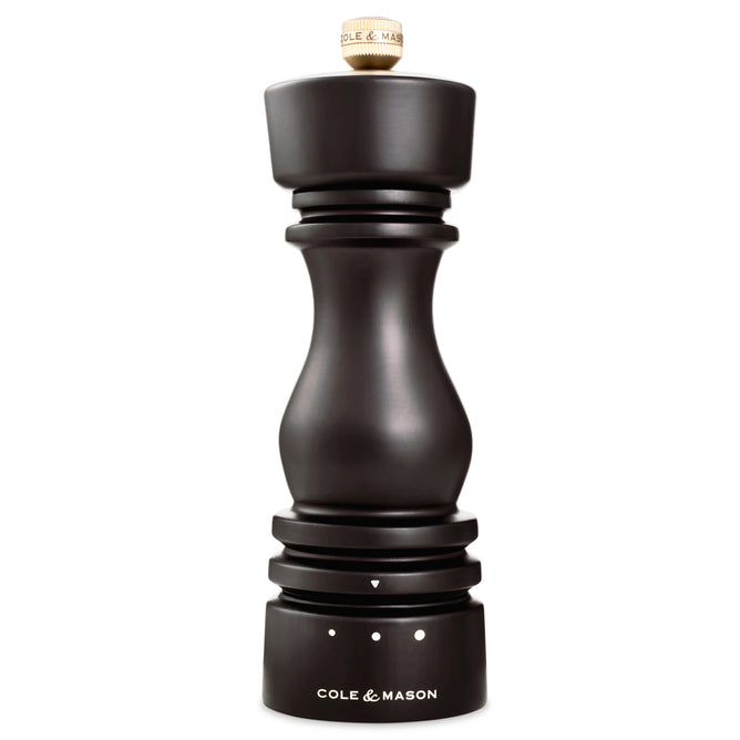 A black Cole & Mason wood salt grinder with a curvy design, ceramic grinding mechanism, silver top adjustment knob, and grind size markings at the base.
