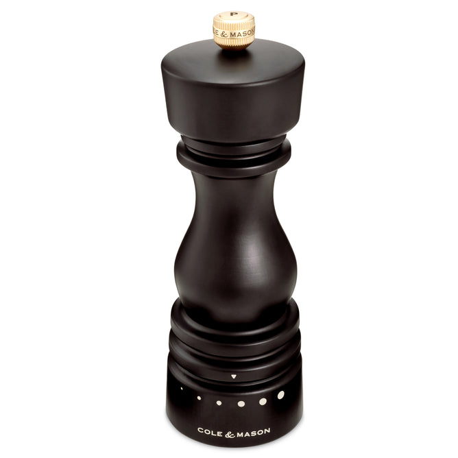 The Cole & Mason Wood Pepper Grinder features a carbon steel grinding mechanism, adjustable grind settings with white dot indicators, and a wooden top knob. Labeled near the bottom, it ensures long-lasting performance.
