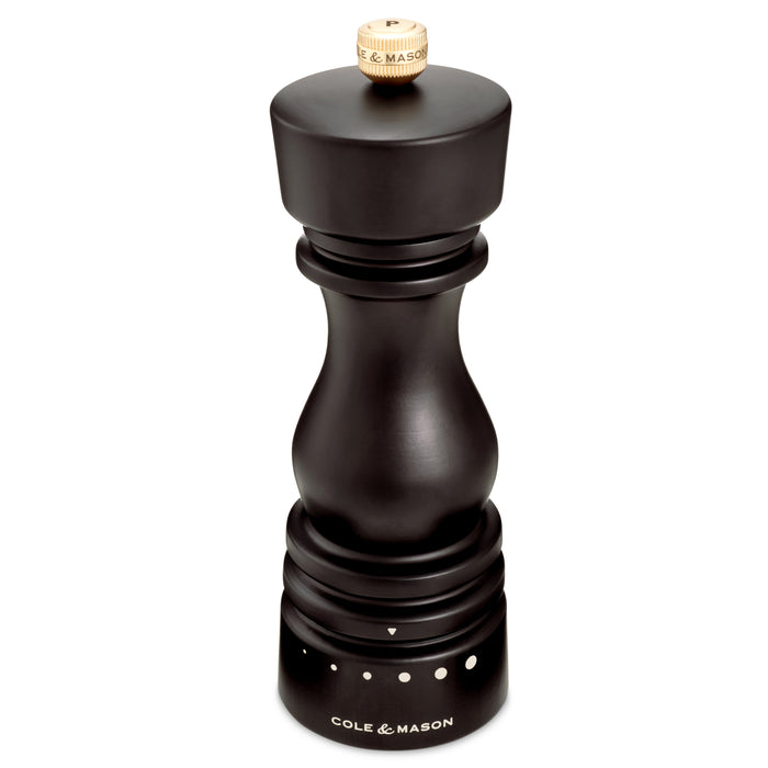 The Cole & Mason Wood Pepper Grinder features a carbon steel grinding mechanism, adjustable grind settings with white dot indicators, and a wooden top knob. Labeled near the bottom, it ensures long-lasting performance.