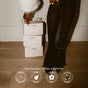 A person in black tights and heels stands by stacked PAUME boxes. Below, text highlights the Hand and Foot Recovery Gift Set: paraben-, sulfate-, silicone-free—ideal for overnight hydration and self-care gifts.