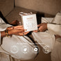 Two people in light robes hold a Hand Treatment Trio Gift Set by PAUME on a brown couch. Icons highlight vegan, natural formulas for hydrated hands and nail care—free from parabens, sulfates, and silicones.