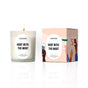 A white Hot Cider Candle by Homesick, made with natural soy wax, sits beside its box decorated with illustrations of raised hands holding drinks in a celebratory toast.