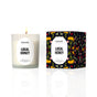 A lit white candle labeled Homesick Hot Cider, made from natural soy wax, stands next to its box, which is decorated with colorful flowers and bees on a dark background.