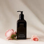 A black pump bottle of Homecourt Laundry Concentrate sits on light fabric, framed by two pink roses, highlighting this eco-friendly detergent made with plant-based cleaning agents.