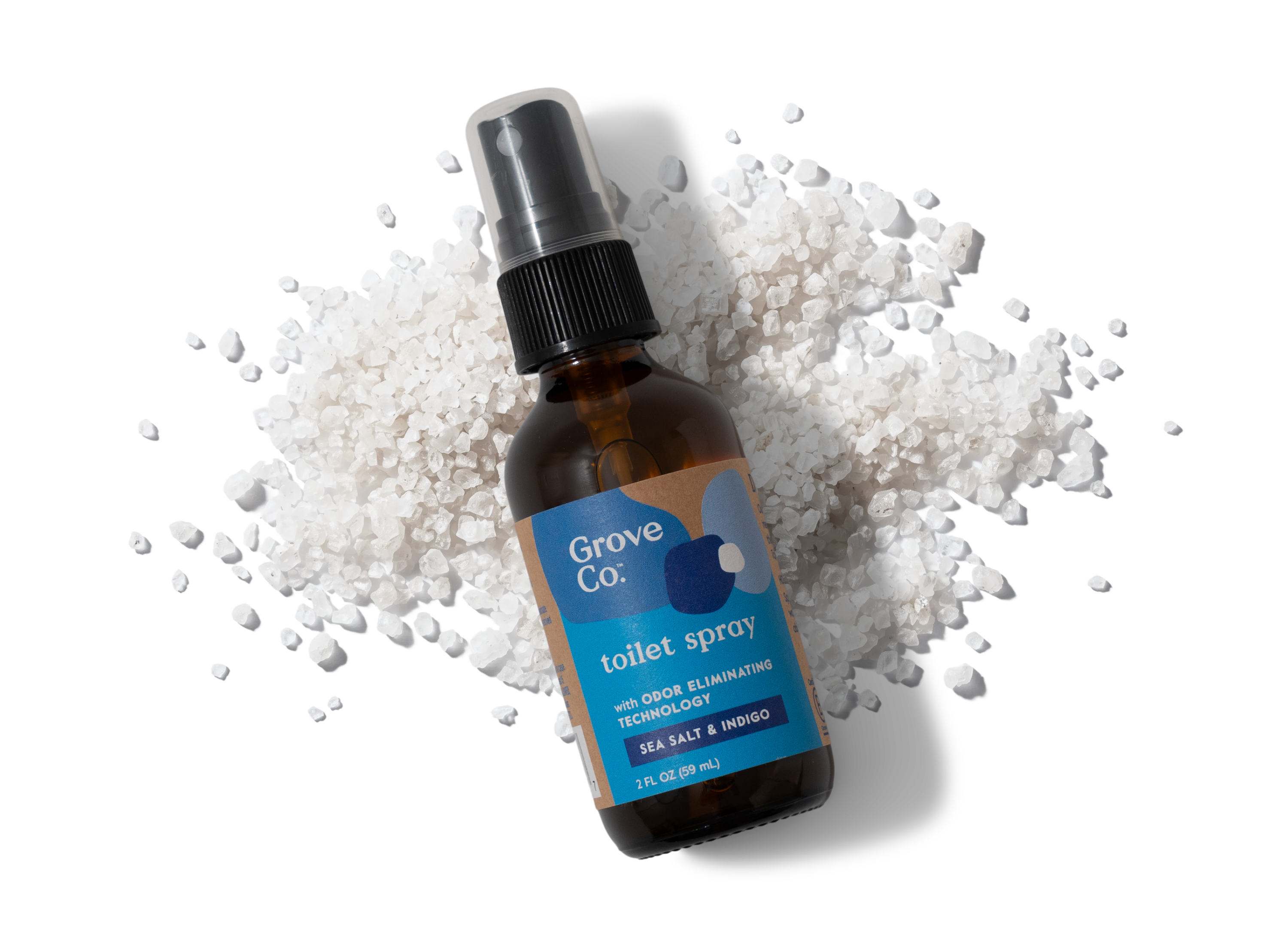 Brown glass bottle of Grove Co. toilet spray on a white background with salt crystals.