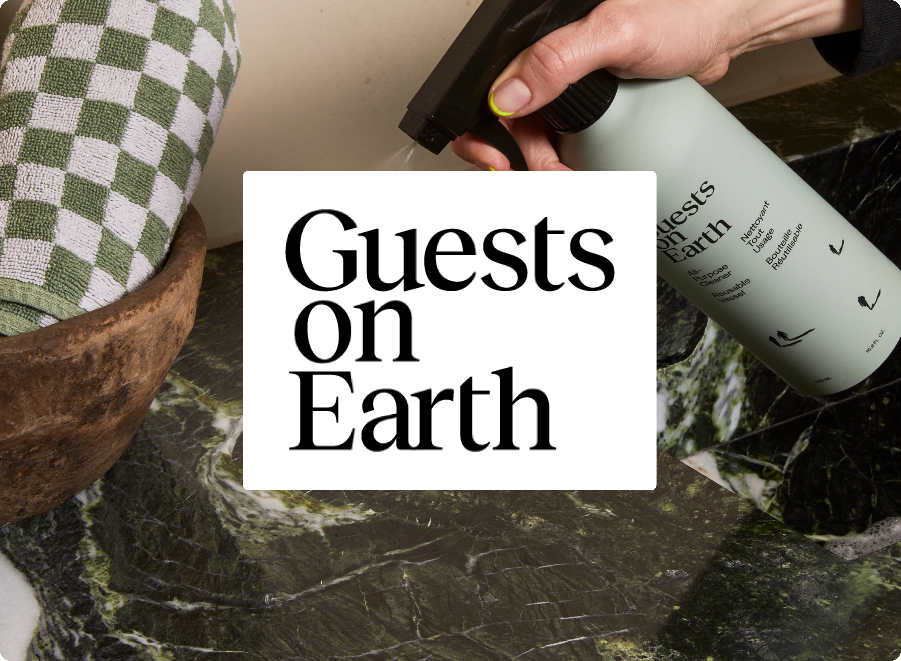 Person holding a bottle labeled 'Guests on Earth' over a checkered towel and marble surface.