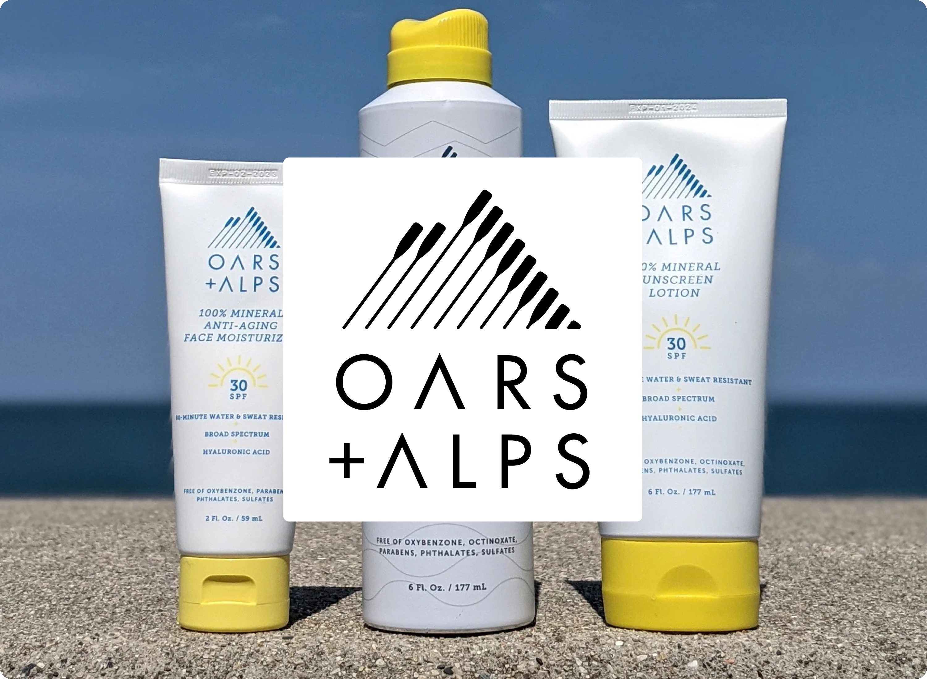 Three Oars + Alps skincare products on a beach with ocean in the background