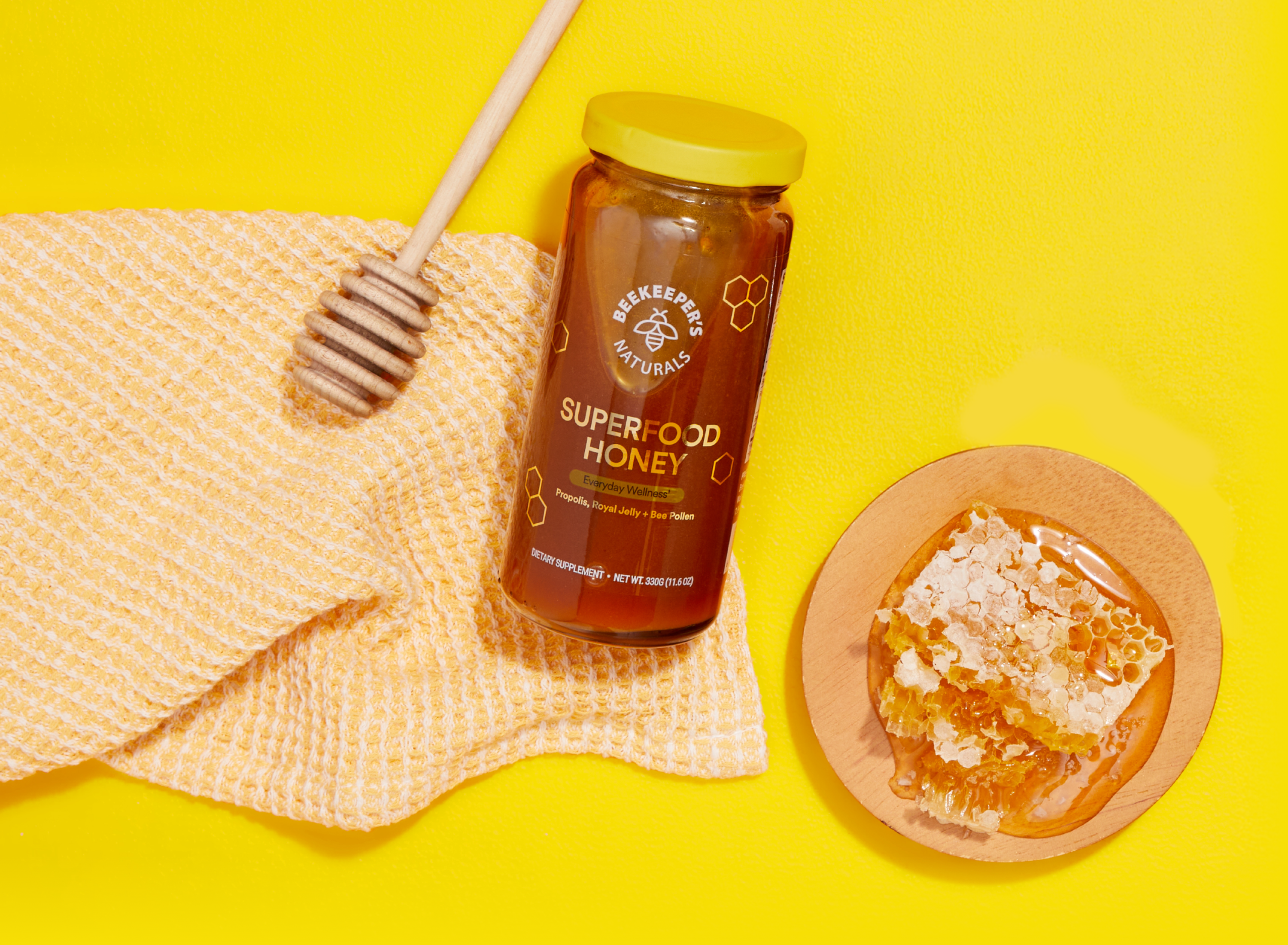 Jar of 'Superfood Honey' with a honeycomb and dipper on a yellow background