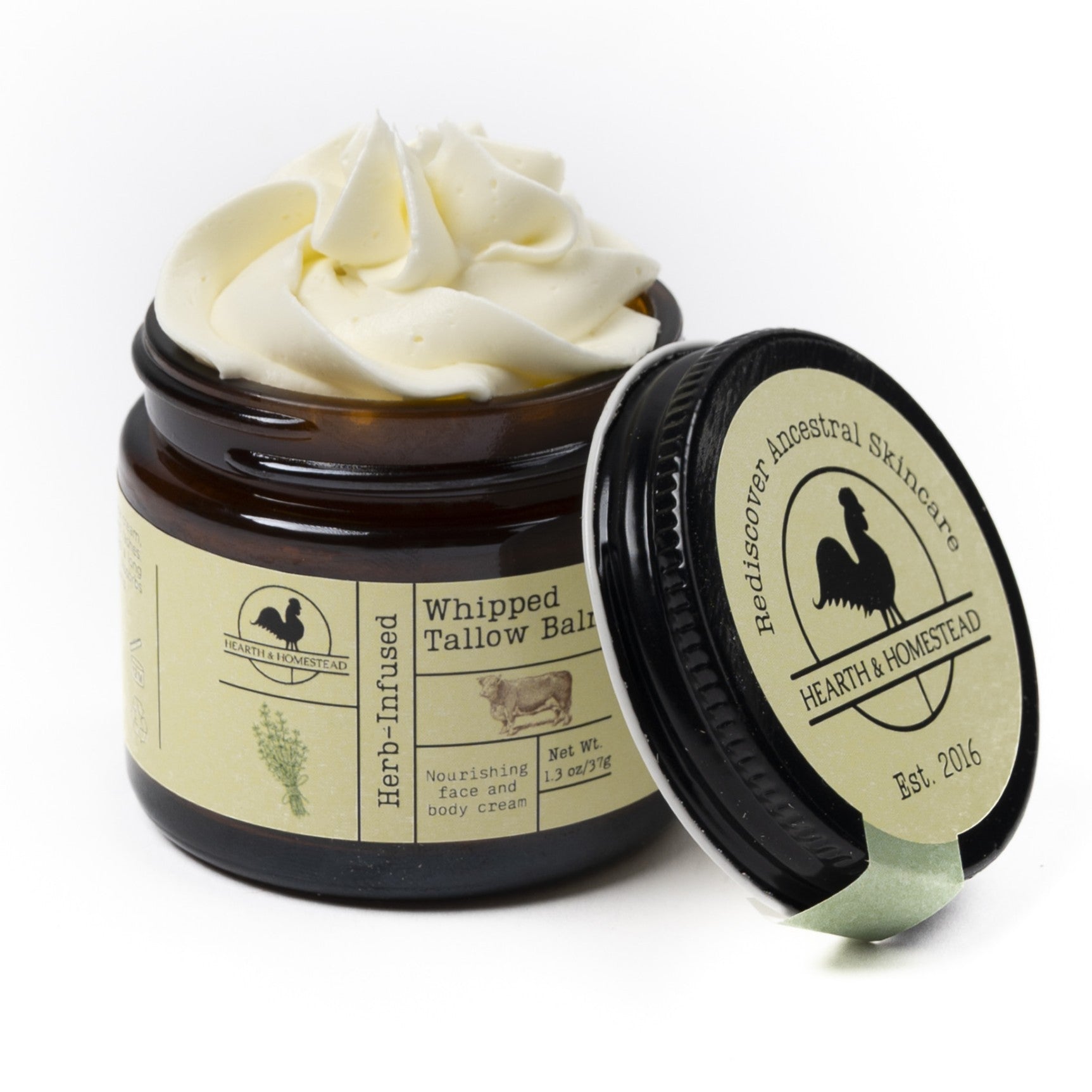 An open jar of Hearth and Homestead Whipped Tallow Balm shows its creamy texture, the lid set aside to display the label and highlight this nourishing, multipurpose skincare product made with grass-fed tallow.