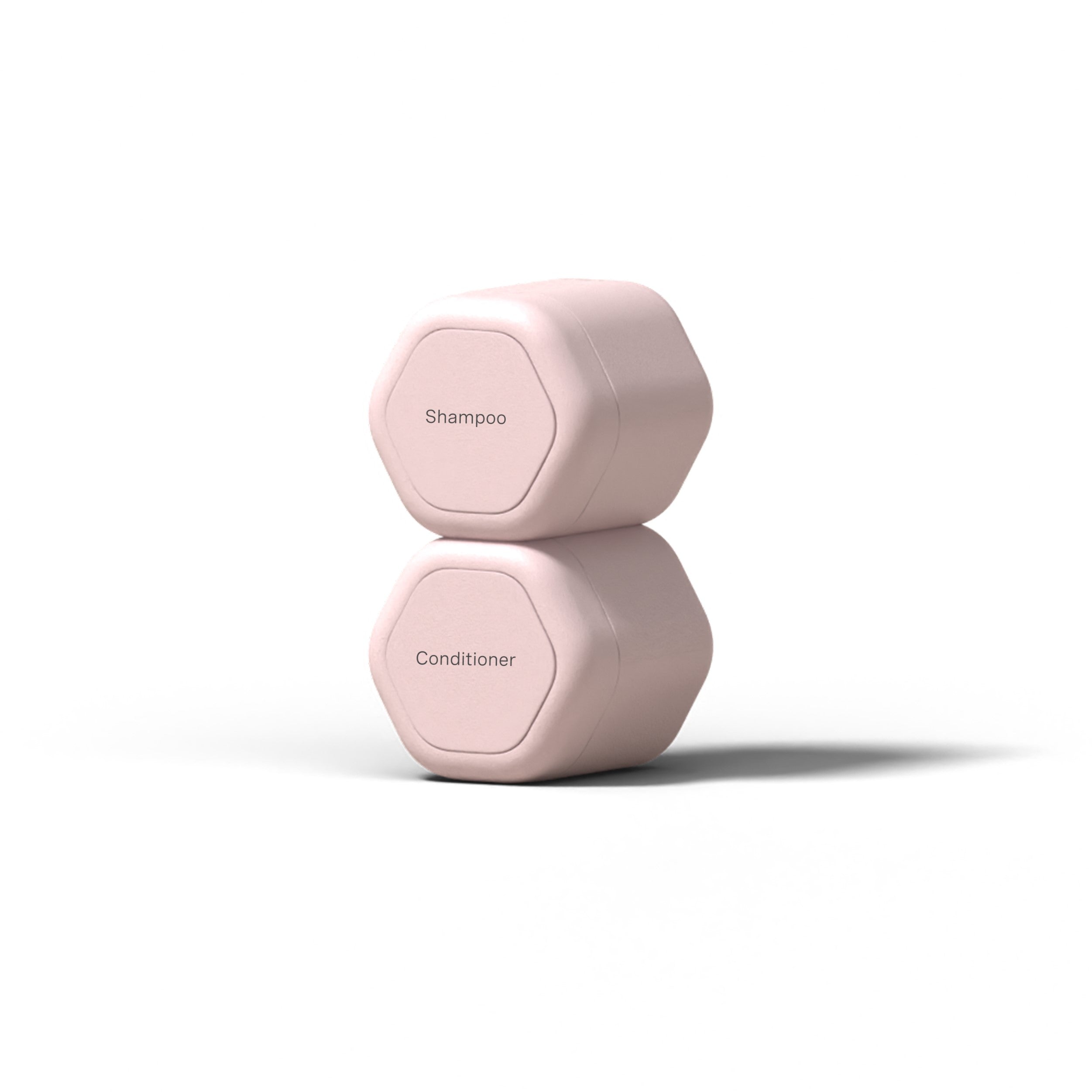 The Cadence Hair Duo Travel Containers, two hexagonal light pink capsules labeled Shampoo and Conditioner, are stacked on a white background—ideal TSA-compliant containers for travel.