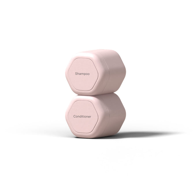 The Cadence Hair Duo Travel Containers, two hexagonal light pink capsules labeled Shampoo and Conditioner, are stacked on a white background—ideal TSA-compliant containers for travel.