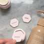 A hand holds a Cadence Labels - Set of 6 container by Cadence with a magnetic Shampoo label, next to containers for Conditioner and a comb icon on marble beside a beige pump bottle of moisturizing shampoo.