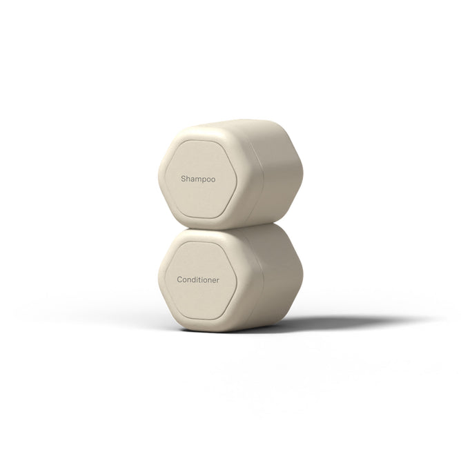 Two hexagonal beige Hair Duo Travel Containers by Cadence, labeled Shampoo and Conditioner, are stacked on a white background—perfect TSA-compliant reusable containers for your next trip.