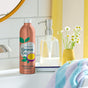 A bottle of Grove Co. Hydrating Hand Soap Refill with passionfruit and white peach design sits on a bathroom sink next to a clear dispenser, complemented by daisies in a vase and a colorful towel, providing plant-based freshness and sustainability.