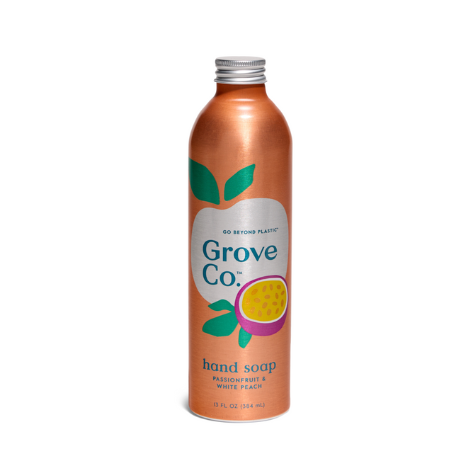 A tall, metallic orange Grove Co. Hydrating Hand Soap Refill bottle, adorned with green leaves and a passionfruit design, is made from recyclable aluminum. Its label reads Passion Fruit & White Peach and advocates for sustainable choices with plant-based ingredients.