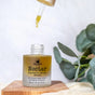 A dropper hovers above a glass bottle labeled Hearth and Homestead Nectar Serum with Natural Retinol and Tallow. Enriched with omega fatty acids, the bottle rests on a wooden surface beside green leaves, while a drop of serum falls from the dropper.