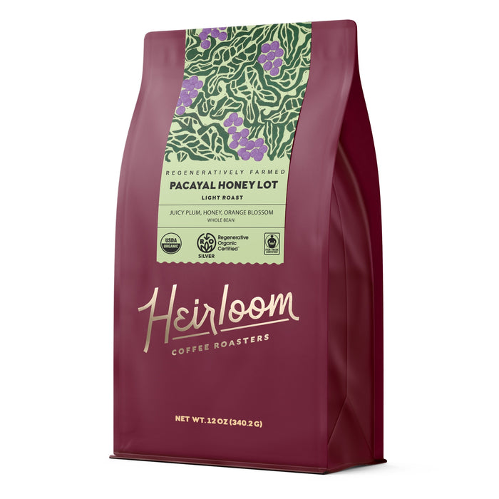 A maroon bag of Heirloom Coffee Roasters Pacayal Honey Lot ROC Whole Bean Coffee, a honey-processed single origin featuring green leaf and fruit art. Showcases regenerative farming and flavors of juicy plum, honey, and orange blossom.