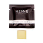 A square black sachet labeled Henné Organics Luxury Lip Balm V2 - Sample and a small beige lip balm piece are displayed on a white background.