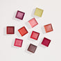 Ten square pigment blocks in vivid reds, pinks, oranges, and yellows inspire the creation of Henné Organics Luxury Lip Balm V2 - Sample, a natural lip balm crafted specifically for sensitive lips.