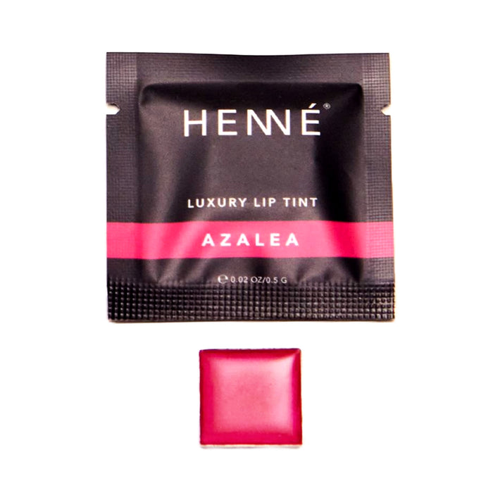 A black sachet labeled Henné Organics Luxury Lip Tint - Sample with a pink stripe, pictured above a square pan holding vibrant, hydrating lip color in a striking pink shade.