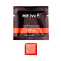 A black sachet labeled Henné Organics Luxury Lip Tint - Sample with a red stripe is shown above a small square of coral-colored organic lip tint.
