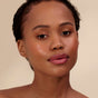 A woman with glowing skin and natural makeup wears Henne Organics Luxury Lip Tint as she looks confidently at the camera, her short dark hair framing her face against a neutral background.