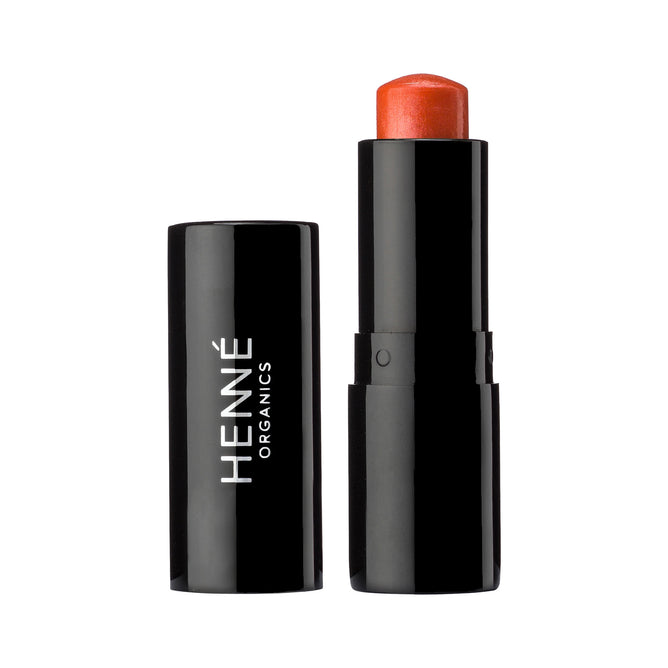 A black tube of Henne Organics Luxury Lip Tint with the cap off reveals a reddish-orange, hydrating lip color. The upright cap sits next to the base, which displays the Henne Organics brand name in white letters.