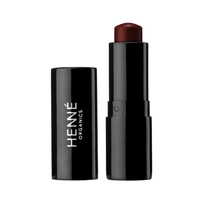 A black tube of Henne Organics Luxury Lip Tint stands upright with its cap beside it. The hydrating lip color is a deep burgundy, and Henne Organics is printed vertically on the cap.