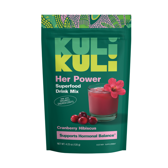 A green pouch of Kuli Kuli Foods Her Power Superfood Drink Mix, Cranberry Hibiscus flavor, featuring a pink drink, cranberries, and hibiscus. The packaging highlights organic ingredients for PMS support and hormonal balance.